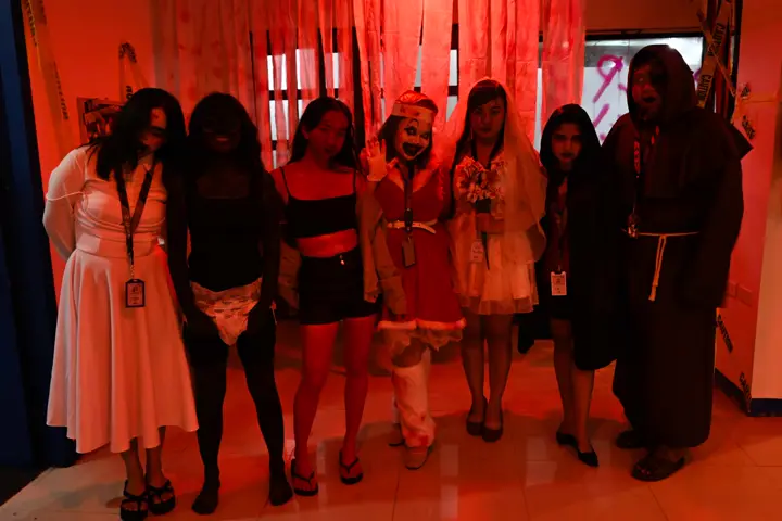 A team of seven in coordinated horror costumes posing under red lights
