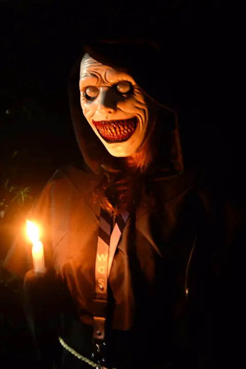A masked figure in a black robe holding a candle