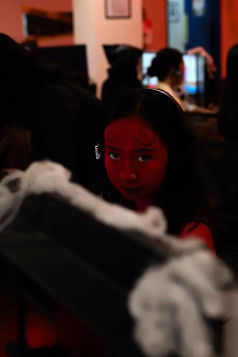 Agent in red face paint behind cobweb decorations at her desk