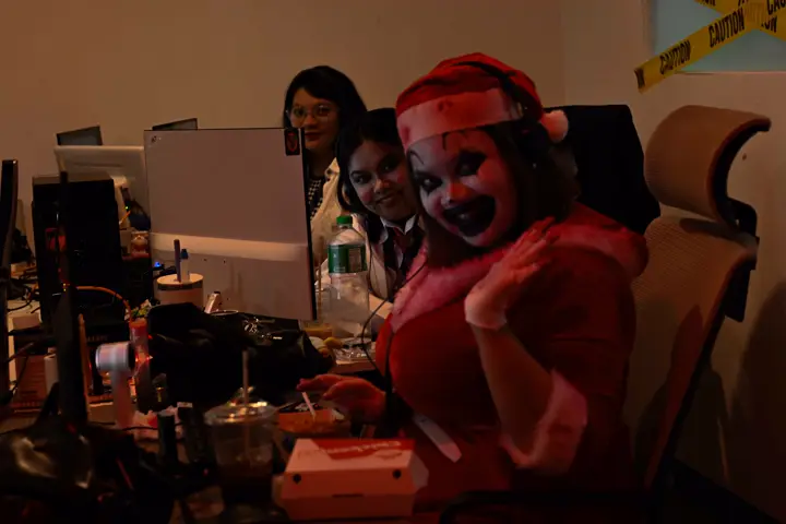 Agent in clown make-up waving from her desk while colleagues work