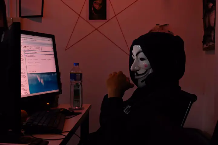 Agent in a mask and hood working at a computer under red light