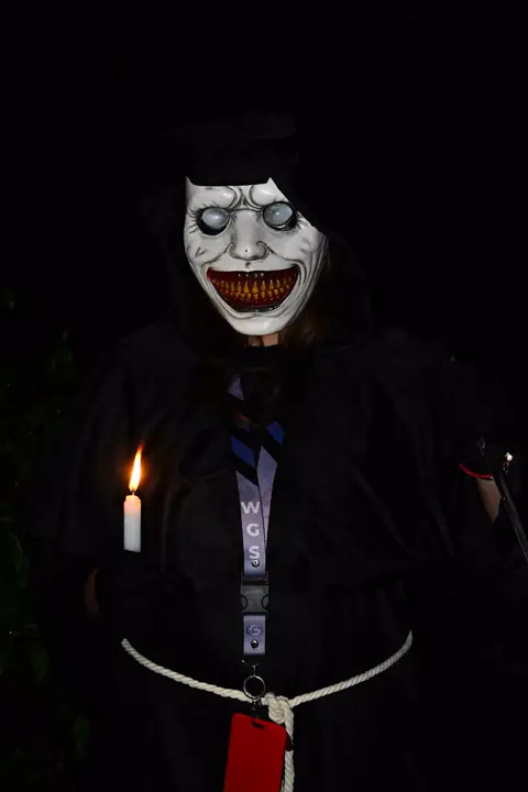 Masked figure in a black robe holding a candle in the dark