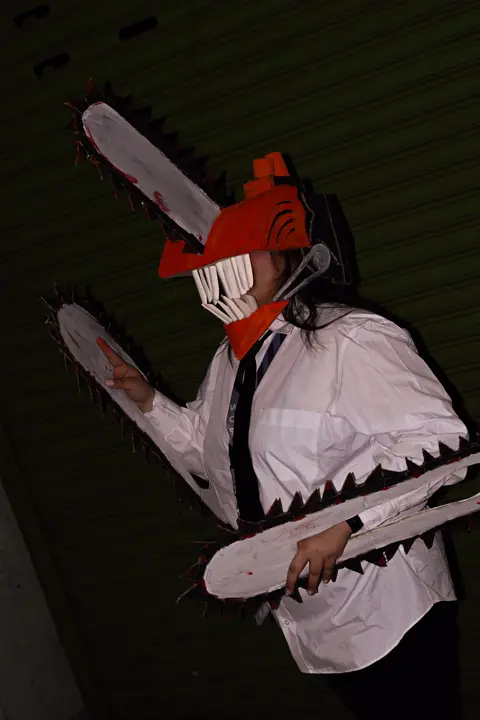 Teammate in a chainsaw-devil costume swinging a prop chainsaw