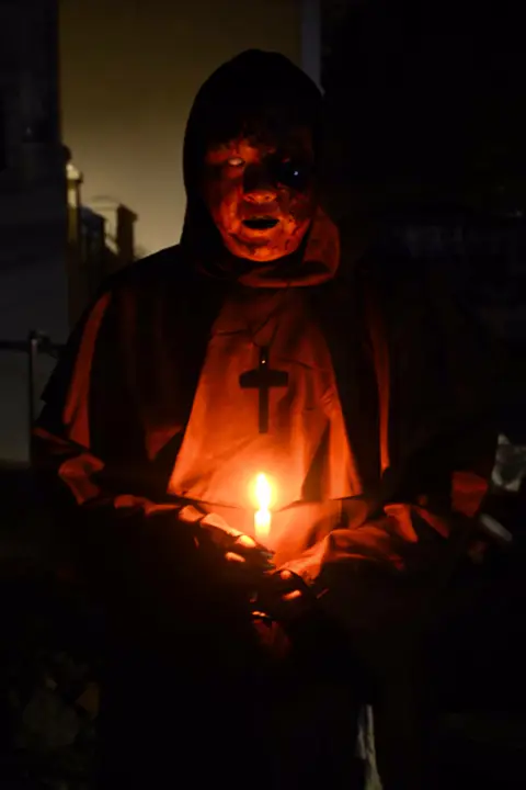 Hooded figure lit by a single candle