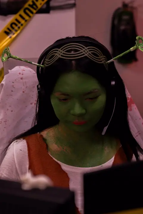 Agent with green face paint and a halo headpiece at her desk